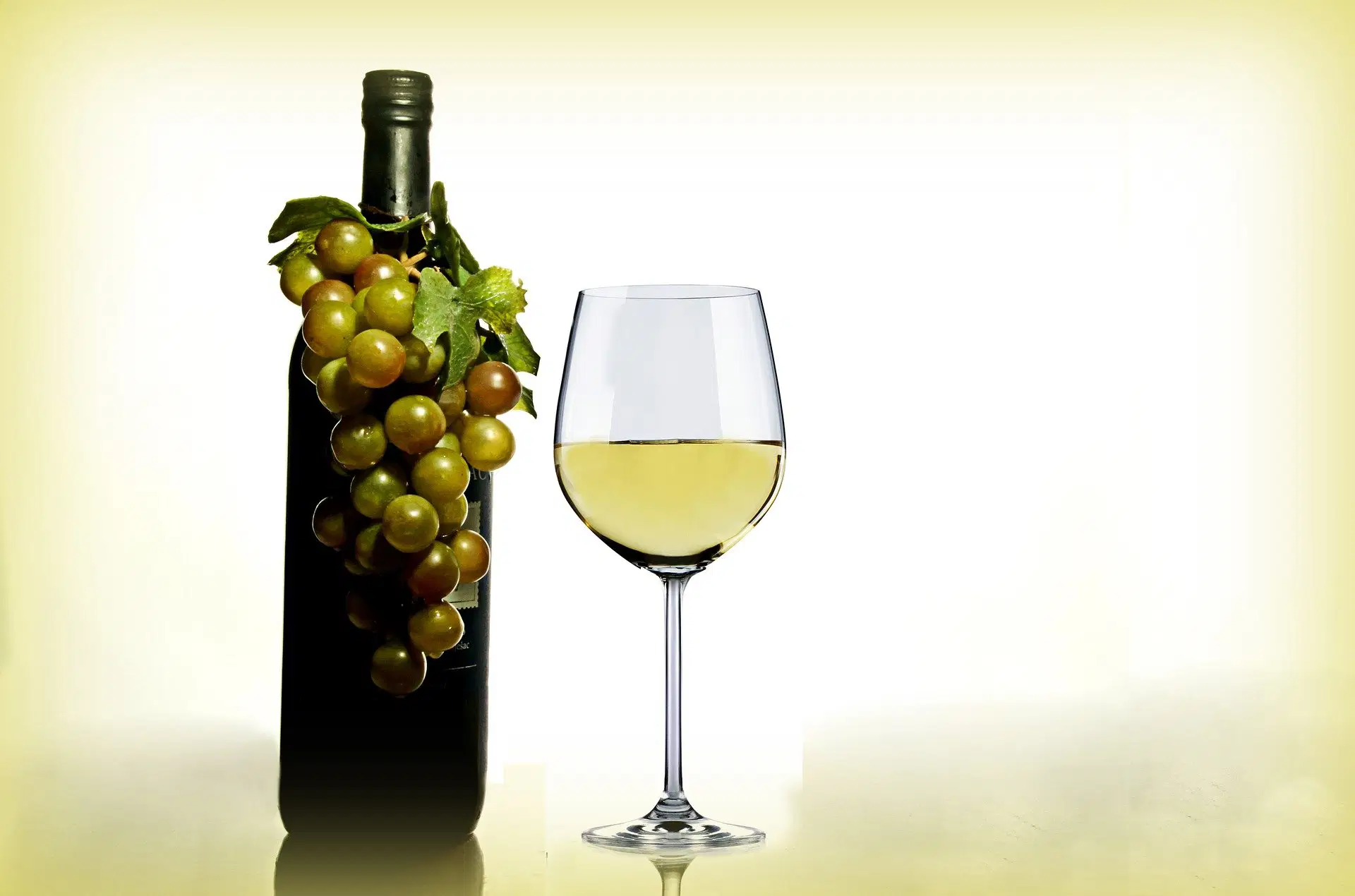Glas Weißwein neben Weinflasche mit Weintrauben