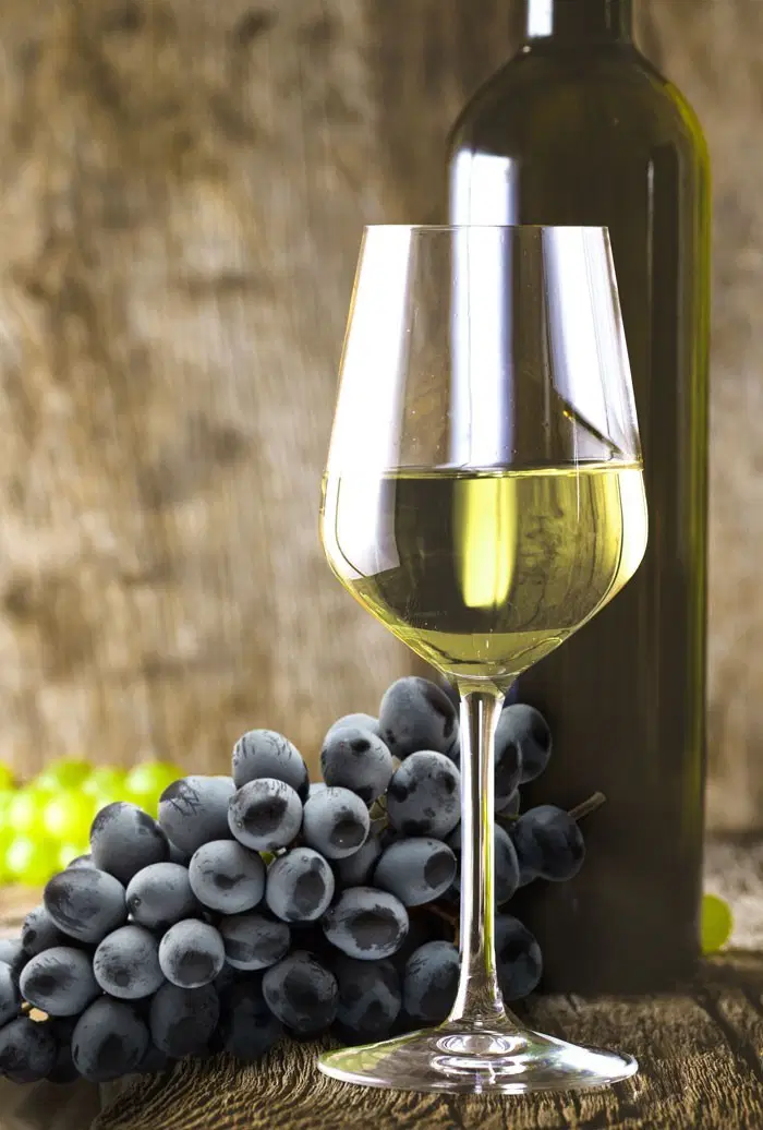 Glas Blanc de Noir mit Weinflasche und Weintrauben im Hintergrund